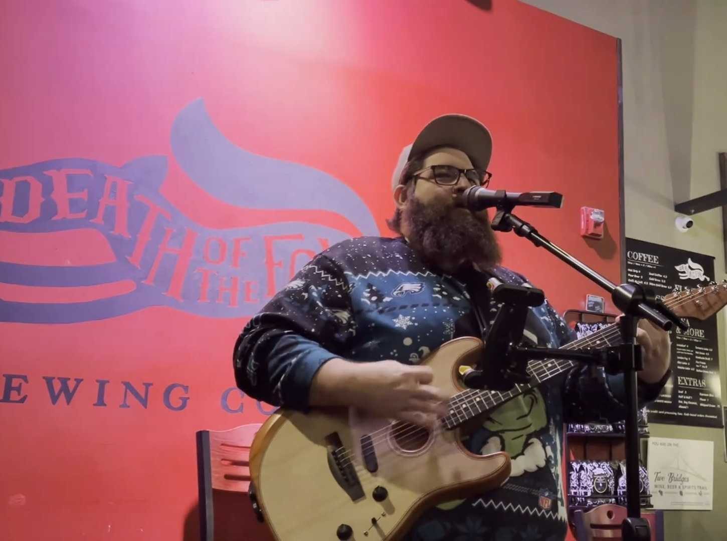 Bearded guitarist singing in front of the red Death of the Fox mural