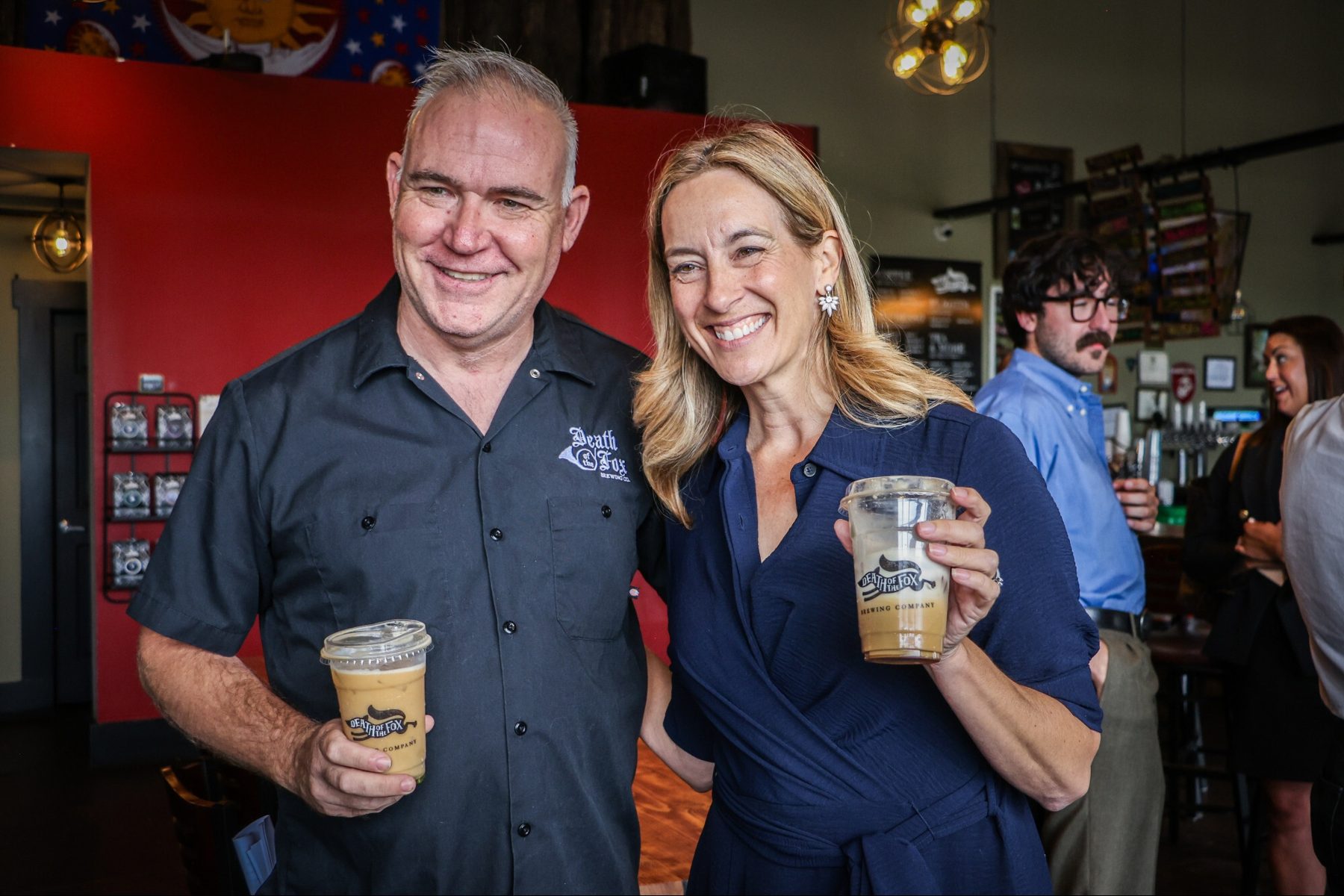 Founder and a guest smiling with Death of the Fox iced coffees in the taproom