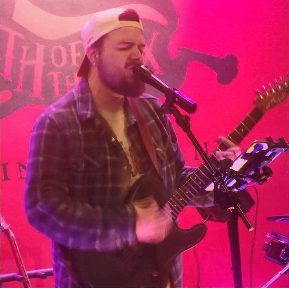 Guitarist singing under pink stage light at Death of the Fox