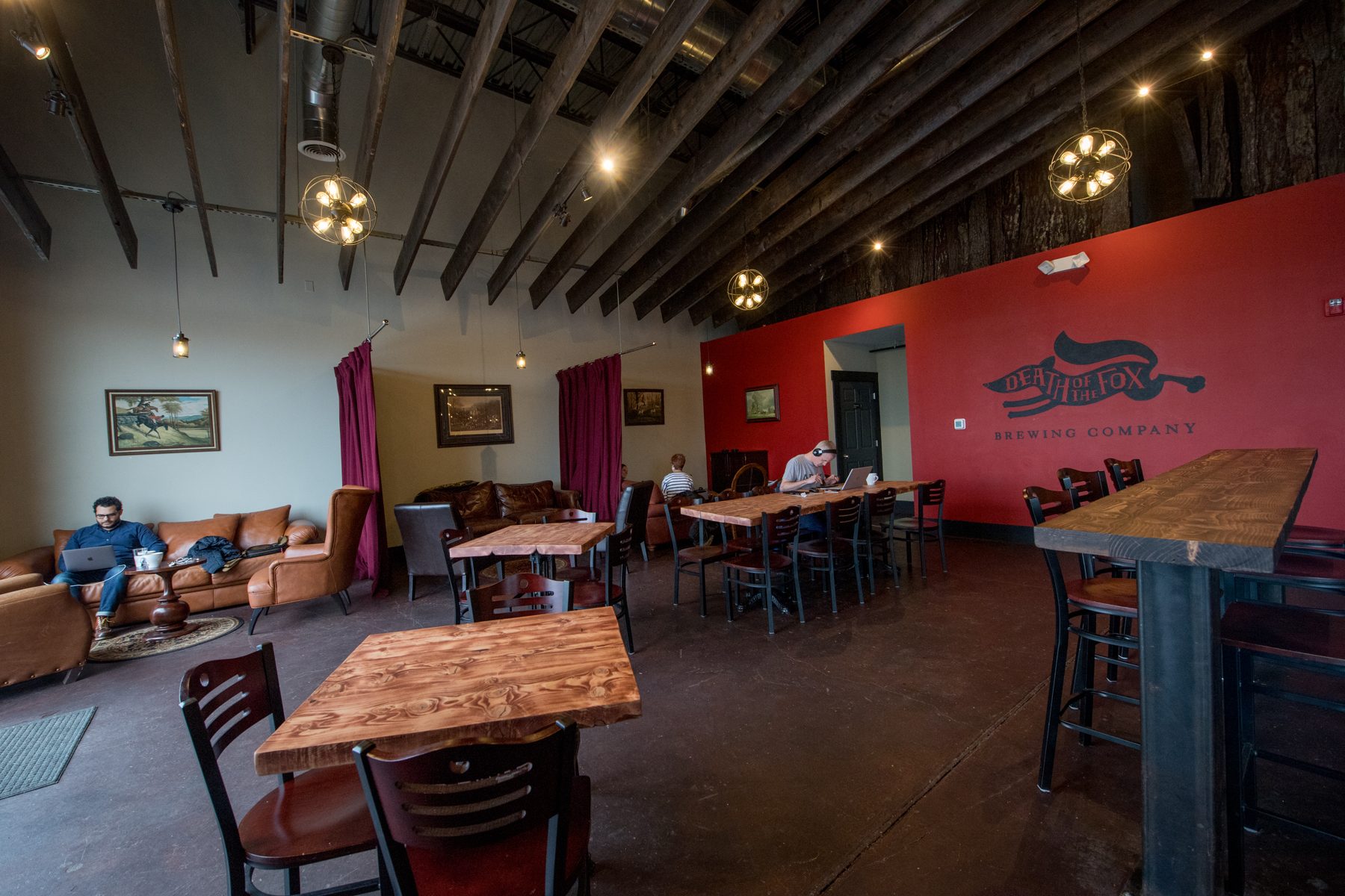 Café section at Death of the Fox with wooden tables beside the red fox mural wall