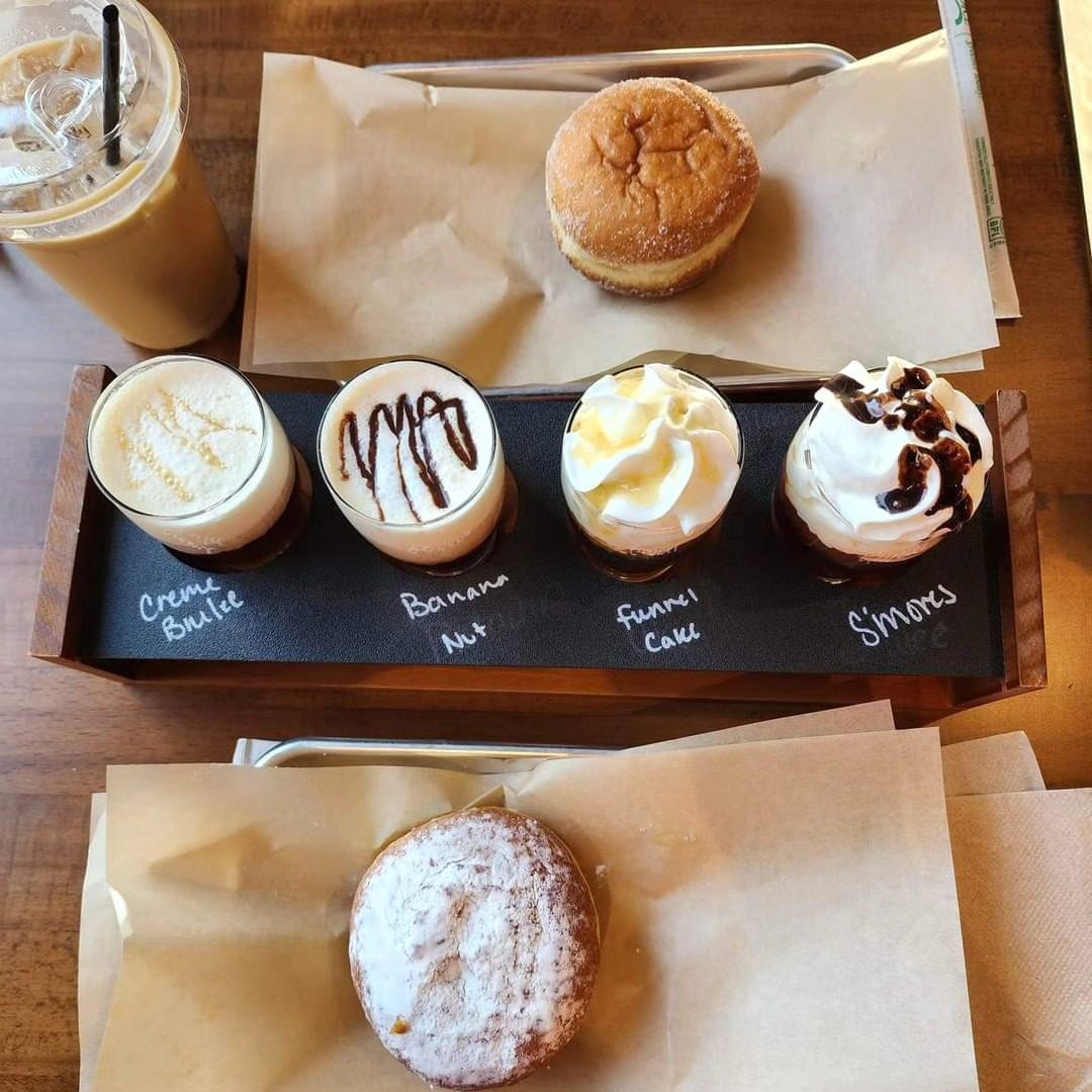 Latte flight board with four whipped-topped lattes beside pastries