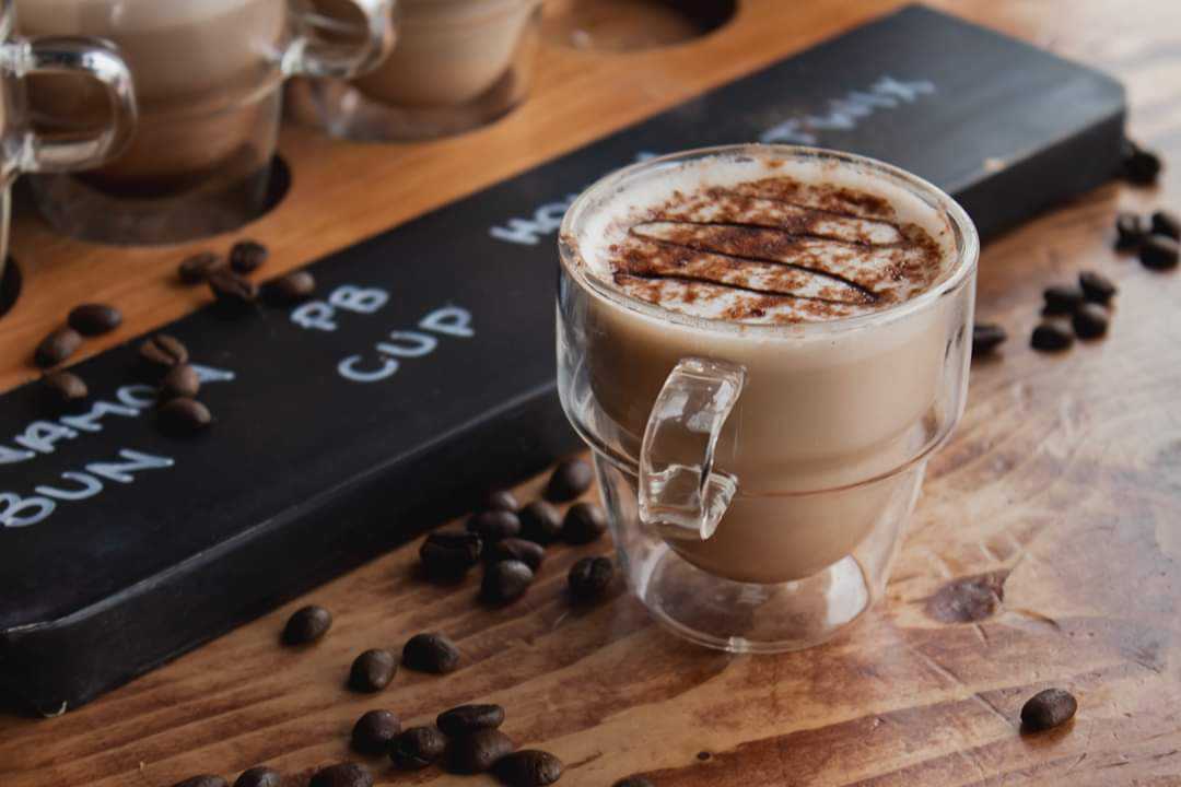 Latte dusted with cinnamon in a glass cup beside a latte flight board with coffee beans