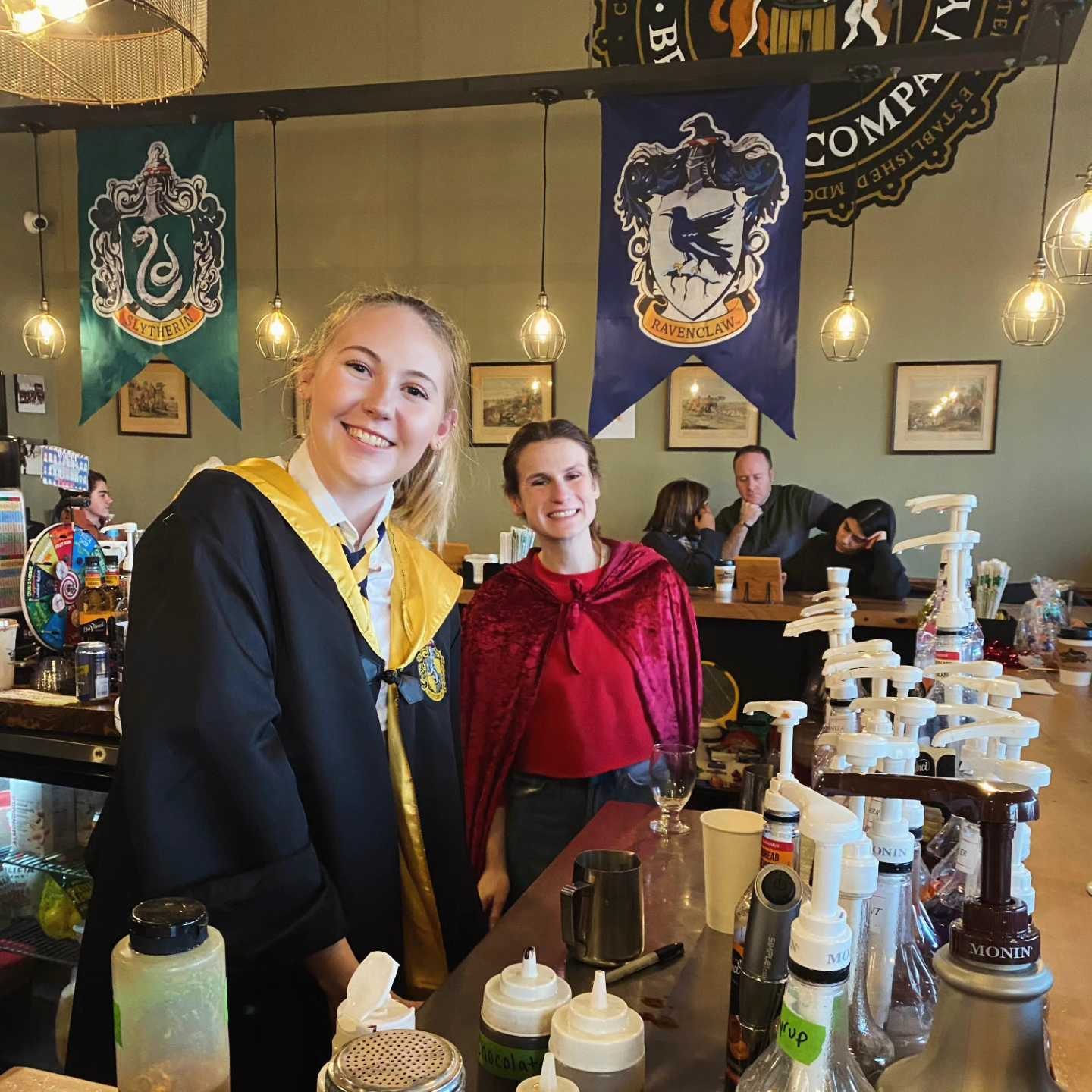 Baristas in wizard robes behind the bar under house banners