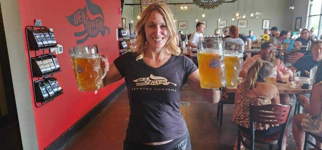 Server holding four beer steins in the Death of the Fox taproom