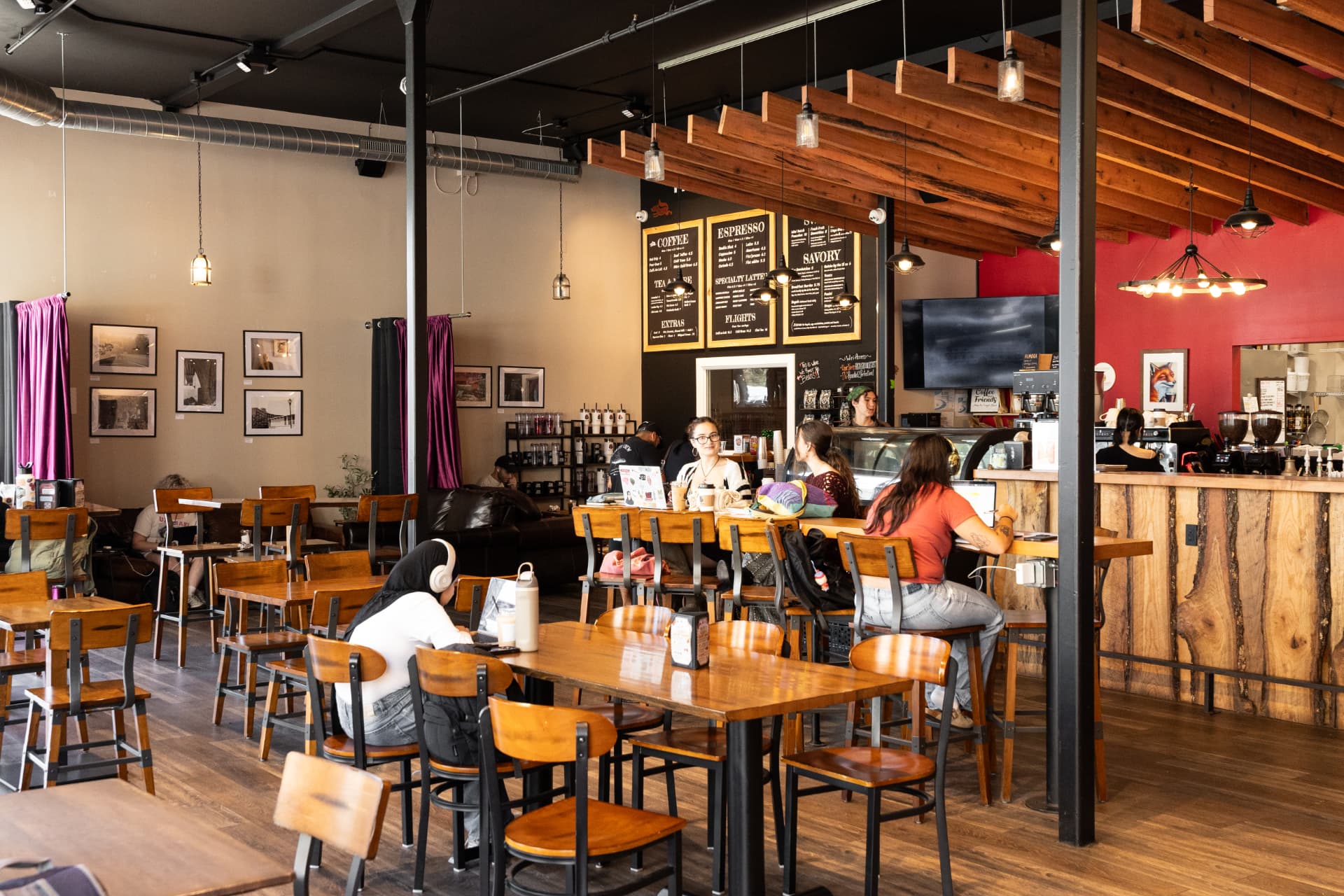 Guests working on laptops at wooden tables in a High Grounds café, with menu boards and the coffee bar behind them