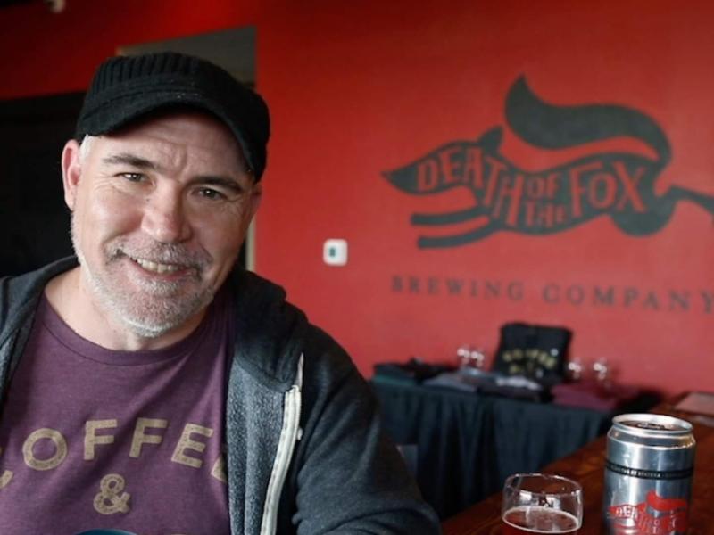 Chuck Garrity smiling at the bar in front of the Death of the Fox mural.